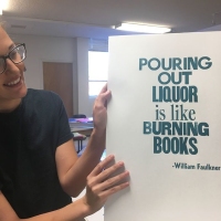 Woman holding a print with a William Faulkner quote on it that says 'pouring out liquor is like burning books.'