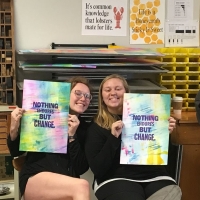 Two students holding prints that say 'nothing endures like change.'