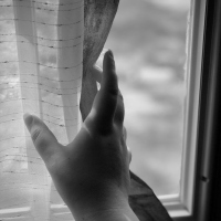 Black and white photo of a hand pulling back a curtain.